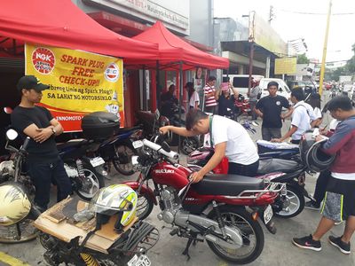 Mechanics checking riders’ motorcycles under red tents outside the store